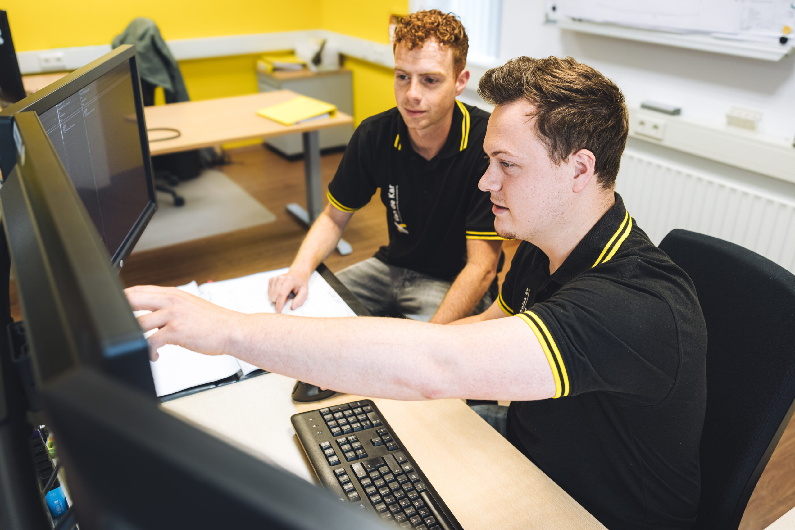 Twee werknemers bij Van de Kar Elektrotechniek die samen kijken naar een document op het scherm.